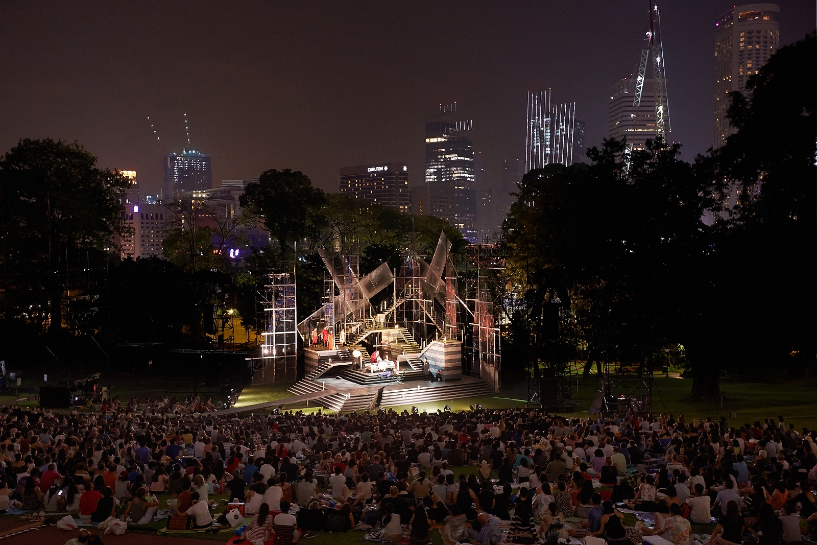 Image of a crowd at Shakespeare in the Park with a massive set in the centre