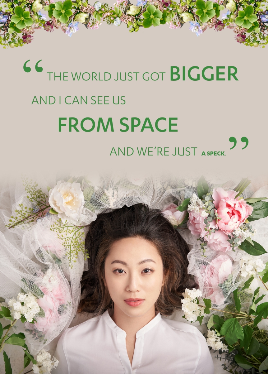 Image of actress Oon Shu An in a white blouse surrounded by lush pink and white flowers. Quote at the top of the image says, the world just got bigger and I can see us from space and we're just a speck.